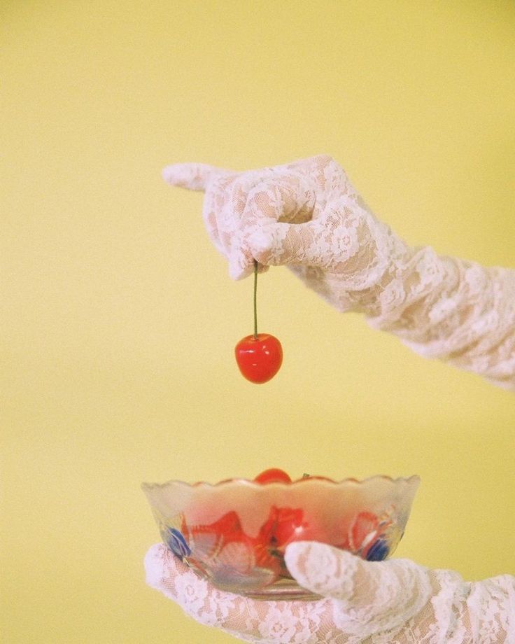 Lace gloved hands holding a cherry and a crystal bowl