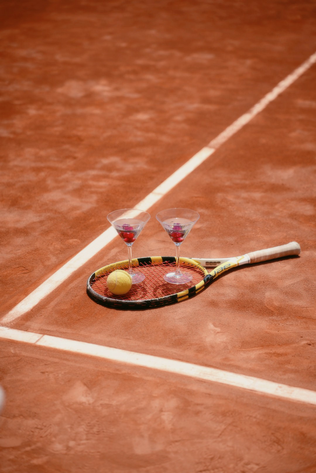 Martini glasses and a racket on a clay tennis court