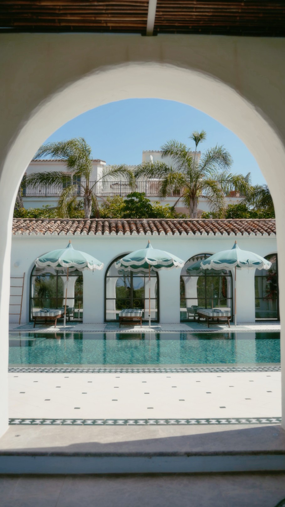 White villa with parasols and a pool seen through an archway